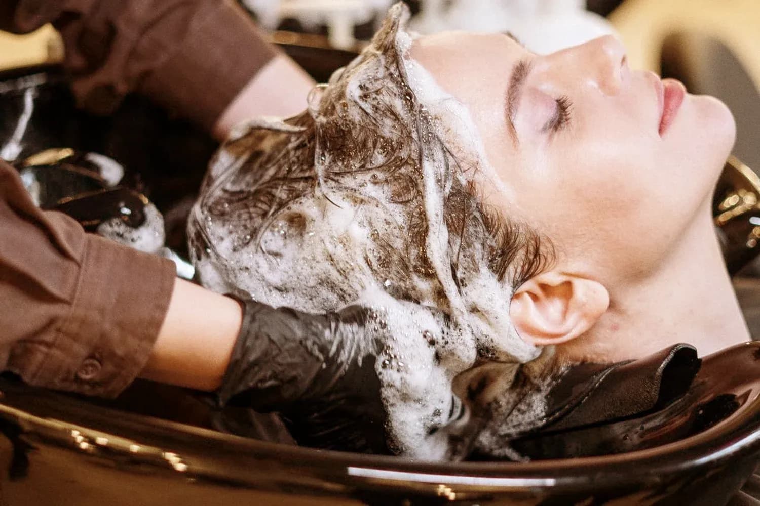 Le mani di una parrucchiera che lavano i capelli a una cliente nel lavatesta del salone.
